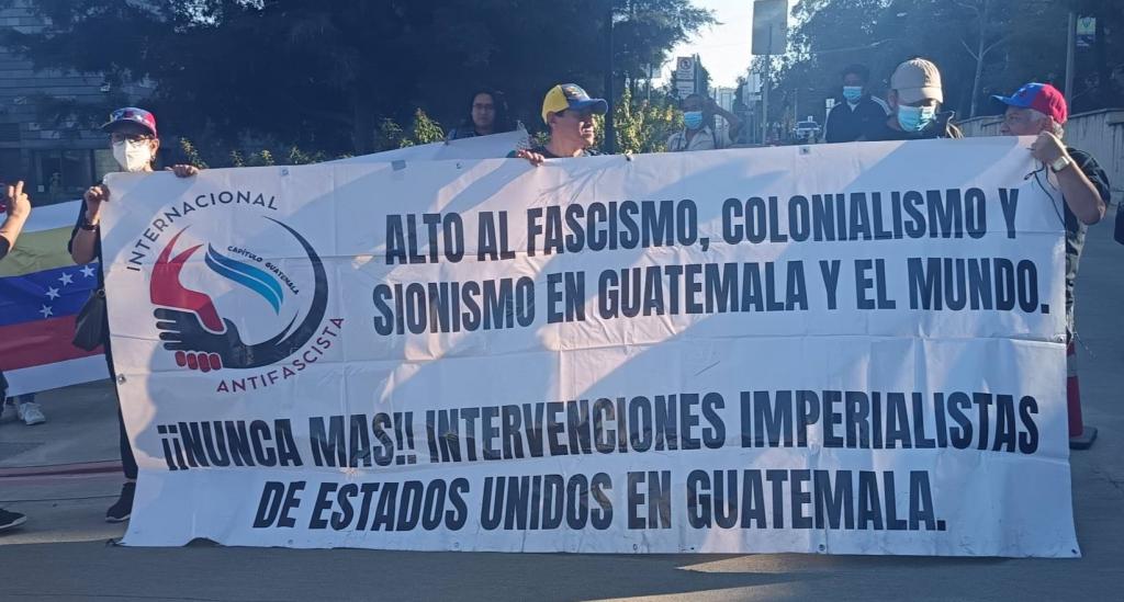 „Állítsuk meg a fasizmust, a gyarmatosítást és a cionizmust Guatemalában és a világban! Le az amerikai beavatkozásokkal Guatemalában!” – követelik a tüntetők az amerikai nagykövetség előtt Guatemalavárosban